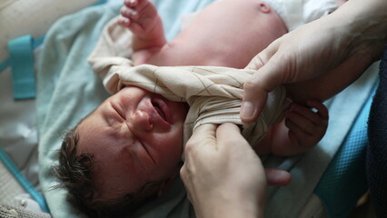 Mother helping newborn baby get dressed, delicate touch on infant's hand, showing care and attention, early moments of bonding and nurturing, tenderness and love in daily routine