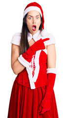 Sticker - Young beautiful caucasian woman wearing santa claus costume surprised pointing with finger to the side, open mouth amazed expression.