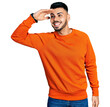 © Krakenimages.com - Young hispanic man with beard wearing casual orange sweater very happy and smiling looking far away with hand over head. searching concept.