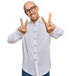 © Krakenimages.com - Bald man with beard wearing business shirt and glasses smiling looking to the camera showing fingers doing victory sign. number two.