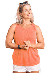 Wall Mural - Middle age fit blonde woman wearing casual summer clothes and sunglasses with hands together and crossed fingers smiling relaxed and cheerful. success and optimistic