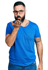 Wall Mural - Hispanic man with beard wearing casual t shirt and glasses looking at the camera blowing a kiss with hand on air being lovely and sexy. love expression.