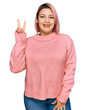 © Krakenimages.com - Hispanic woman with pink hair wearing casual winter sweater smiling looking to the camera showing fingers doing victory sign. number two.