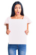 © Krakenimages.com - Young beautiful latin girl holding blank empty banner scared and amazed with open mouth for surprise, disbelief face