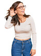 © Krakenimages.com - Young brunette woman wearing casual clothes and glasses smiling with hand over ear listening an hearing to rumor or gossip. deafness concept.