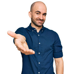 Wall Mural - Young hispanic man wearing casual clothes smiling cheerful offering palm hand giving assistance and acceptance.