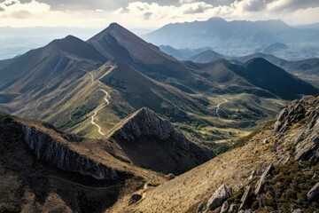 Wall Mural - Scenic mountainous landscape with winding paths, rugged peaks, and distant valleys under a cloudy sky.