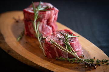 Raw Filet Mignon on a cutting board with rosemary and black pepper.