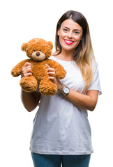 Wall Mural - Young beautiful woman holding teddy bear plush over isolated background with a happy face standing and smiling with a confident smile showing teeth