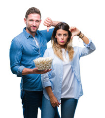 Canvas Print - Young couple in love eating popcorn over isolated background with angry face, negative sign showing dislike with thumbs down, rejection concept