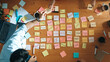 © Summit Art Creations - Top view of skilled business people discuss plan at meeting room while writing idea at sticky notes and stick at whiteboard. Group of diverse team working together to planning strategy. Convocation.