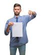 © Krakenimages.com - Young handsome man holding blank paper over isolated background with angry face, negative sign showing dislike with thumbs down, rejection concept