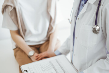 Doctor and patient in clinic. Friendly physician examining a young woman with a one hand while keeping a clipboard with medical records in another. Medicine concept