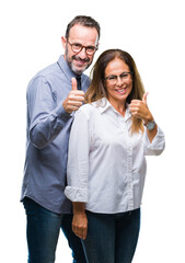 Middle age hispanic couple in love wearing glasses over isolated background doing happy thumbs up gesture with hand. Approving expression looking at the camera with showing success.