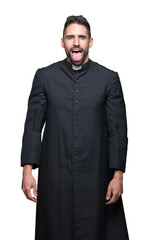 Young Christian priest over isolated background sticking tongue out happy with funny expression. Emotion concept.