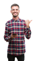 Poster - Young hipster adult man holding smartphone pointing and showing with thumb up to the side with happy face smiling