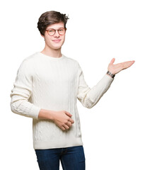 Young handsome man wearing glasses over isolated background smiling cheerful presenting and pointing with palm of hand looking at the camera.