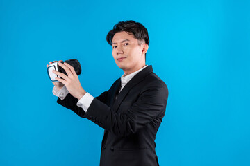 Asian businessman looking at camera holding VR connecting to financial report in futuristic metaverse business data analytics communication technology virtual reality in blue copyspace. Contrivance.