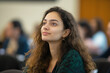 © BetterPhoto - A young woman with curly brown hair, attentively listening during a seminar, her gaze focused upward, capturing a moment of inspiration and learning.