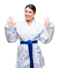 Wall Mural - Young beautiful woman wearing karate kimono uniform over isolated background showing and pointing up with fingers number eight while smiling confident and happy.