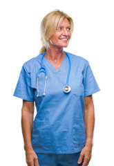 Poster - Middle age blonde nurse surgeon doctor woman over isolated background looking away to side with smile on face, natural expression. Laughing confident.