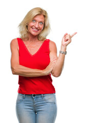 Sticker - Middle age blonde woman over isolated background with a big smile on face, pointing with hand and finger to the side looking at the camera.