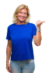 Wall Mural - Middle age blonde woman over isolated background smiling with happy face looking and pointing to the side with thumb up.