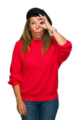 Wall Mural - Middle age adult woman wearing fashion beret over isolated background doing ok gesture shocked with surprised face, eye looking through fingers. Unbelieving expression.