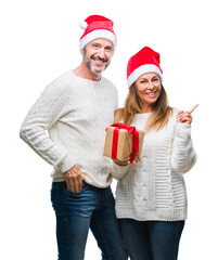 Canvas Print - Middle age hispanic couple wearing christmas hat and holding gift over isolated background very happy pointing with hand and finger to the side