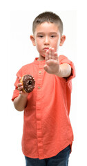 Sticker - Dark haired little child eating doughnut with open hand doing stop sign with serious and confident expression, defense gesture