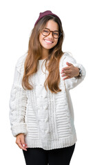 Wall Mural - Young beautiful brunette hipster woman wearing glasses and winter hat over isolated background smiling friendly offering handshake as greeting and welcoming. Successful business.