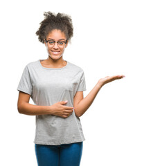 Poster - Young afro american woman wearing glasses over isolated background smiling cheerful presenting and pointing with palm of hand looking at the camera.