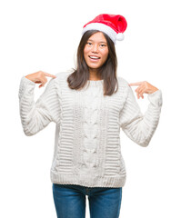 Poster - Young asian woman wearing christmas hat over isolated background looking confident with smile on face, pointing oneself with fingers proud and happy.