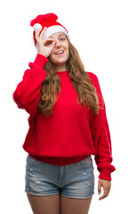 Poster - Young blonde woman wearing santa claus hat with happy face smiling doing ok sign with hand on eye looking through fingers