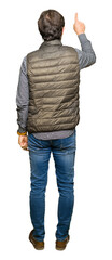 Middle age handsome man wearing winter vest Posing backwards pointing behind with finger hand