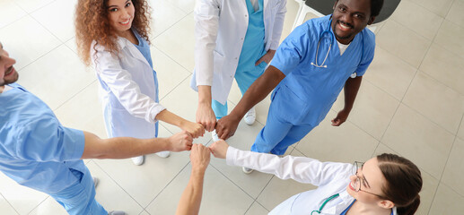 Canvas Print - Group of doctors putting hands together in clinic, top view. Unity concept