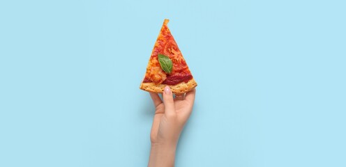 Hand holding slice of tasty pizza on light blue background