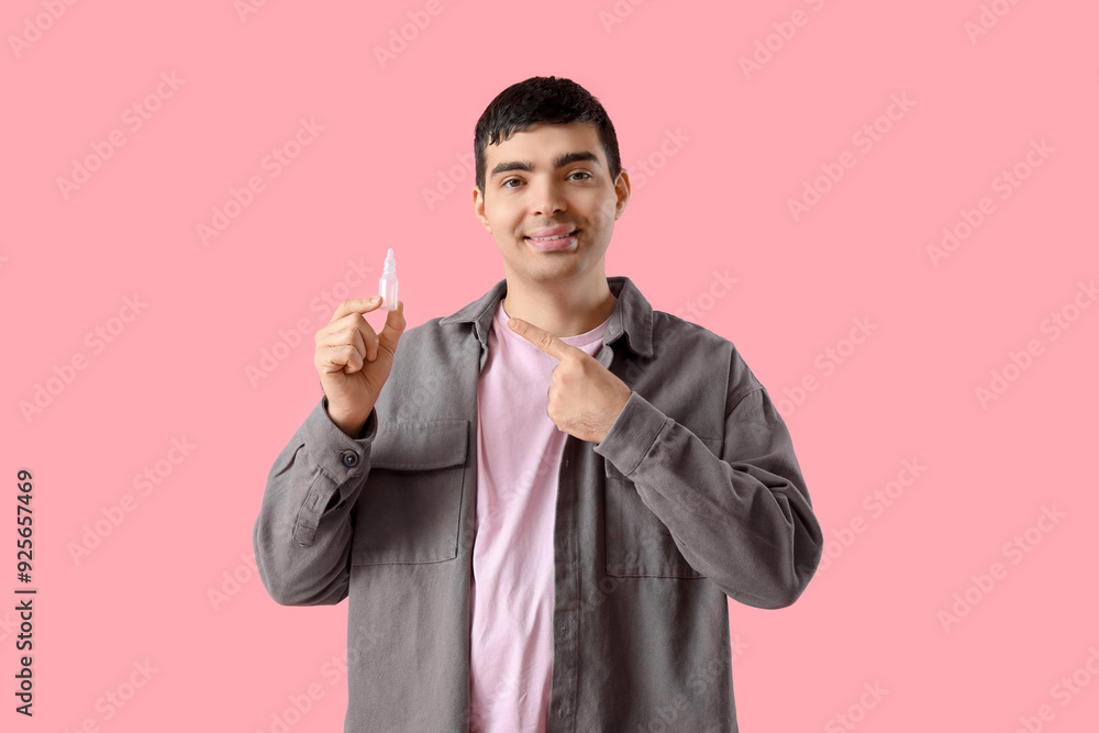 Young man pointing at nasal drops on pink background