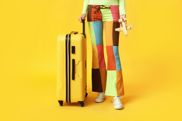 Poster - Young woman with suitcase and toy airplane on yellow background. Travel concept