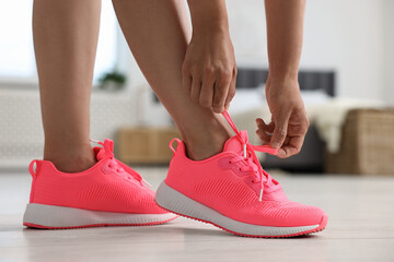 Wall Mural - Woman tying shoelace of pink sneaker indoors, closeup