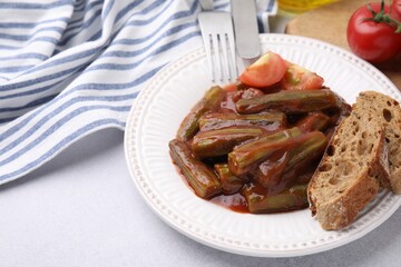 Tasty stew with okra, tomato sauce and bread on white table, closeup. Space for text