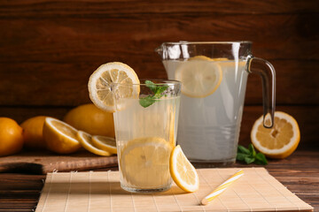 Wall Mural - Glass and jug of fresh lemonade with mint on wooden background