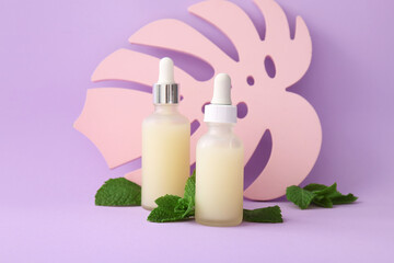 Wall Mural - Bottles of essential oil, plaster palm leaf and mint leaves on lilac background