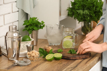 Wall Mural - Young woman cutting mint leaves for preparation mojito in kitchen