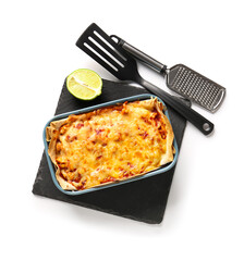 Wall Mural - Baking dish with tasty enchilada, lime and kitchen utensils on white background