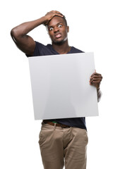 Poster - Young african american man holding a banner stressed with hand on head, shocked with shame and surprise face, angry and frustrated. Fear and upset for mistake.