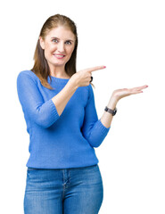 Beautiful middle age mature woman wearing winter sweater over isolated background amazed and smiling to the camera while presenting with hand and pointing with finger.