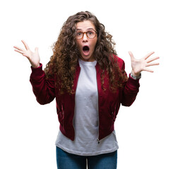 Poster - Beautiful brunette curly hair young girl wearing jacket and glasses over isolated background celebrating crazy and amazed for success with arms raised and open eyes screaming excited. Winner concept