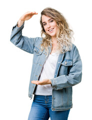 Wall Mural - Beautiful young blonde woman wearing denim jacket over isolated background gesturing with hands showing big and large size sign, measure symbol. Smiling looking at the camera. Measuring concept.