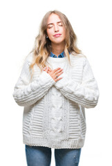 Wall Mural - Beautiful young blonde woman wearing winter sweater over isolated background smiling with hands on chest with closed eyes and grateful gesture on face. Health concept.